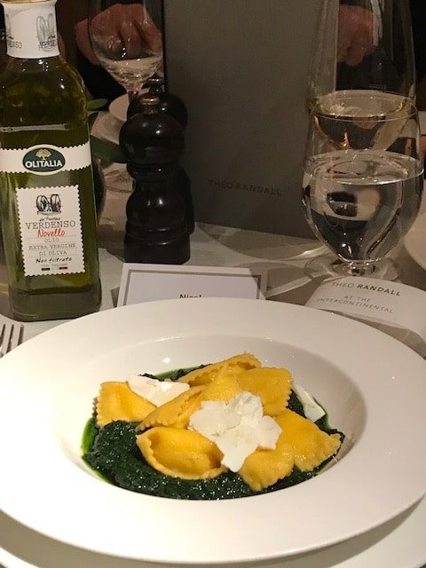 plate of ravioli on black kale sauce next to a bottle of Novello olive oil