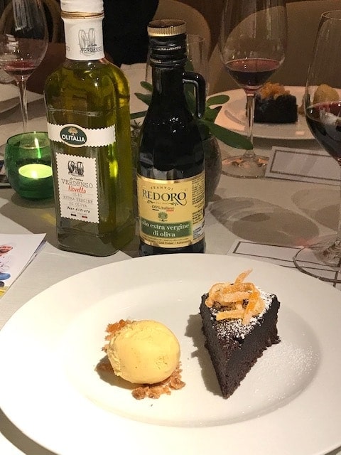 A slice of Sicilian chocolate cake and a scoop of ice cream on a plate with two bottles of olive oil