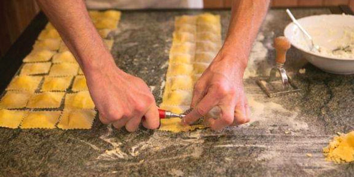 Hands cutting ravioli from fresh pasta.