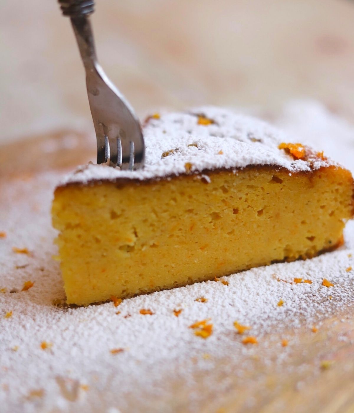 A metal fork going into a slice of orange and almond cake.