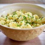 Image of potato salad with chopped parsley in large yellow bowl.