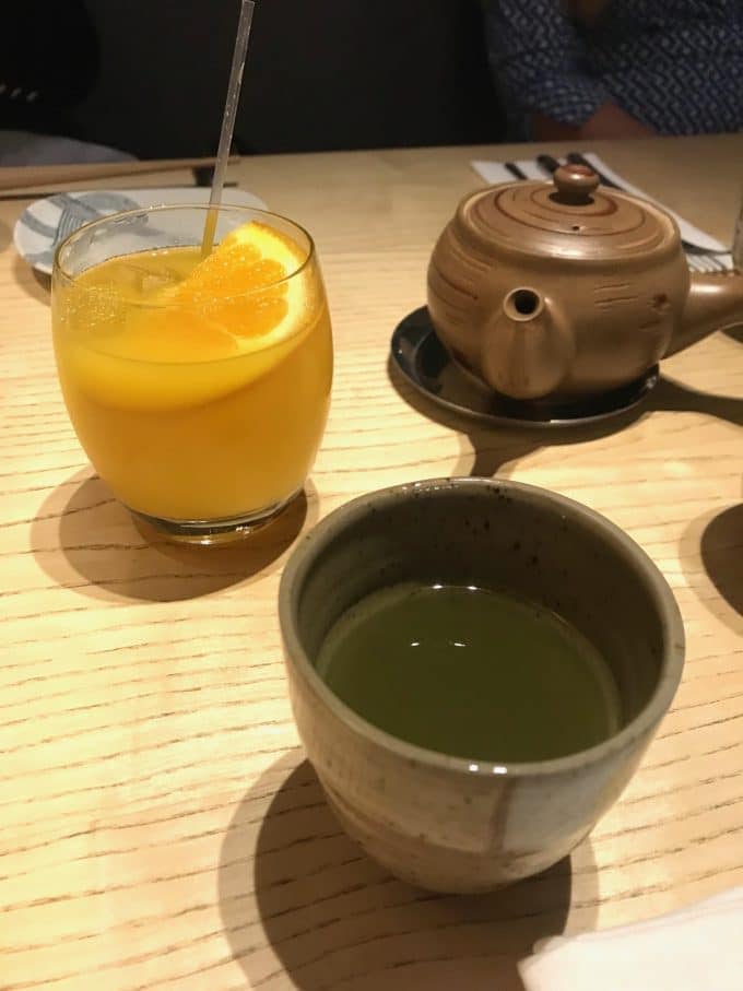 Glass of orange juice and cup of matcha tea.