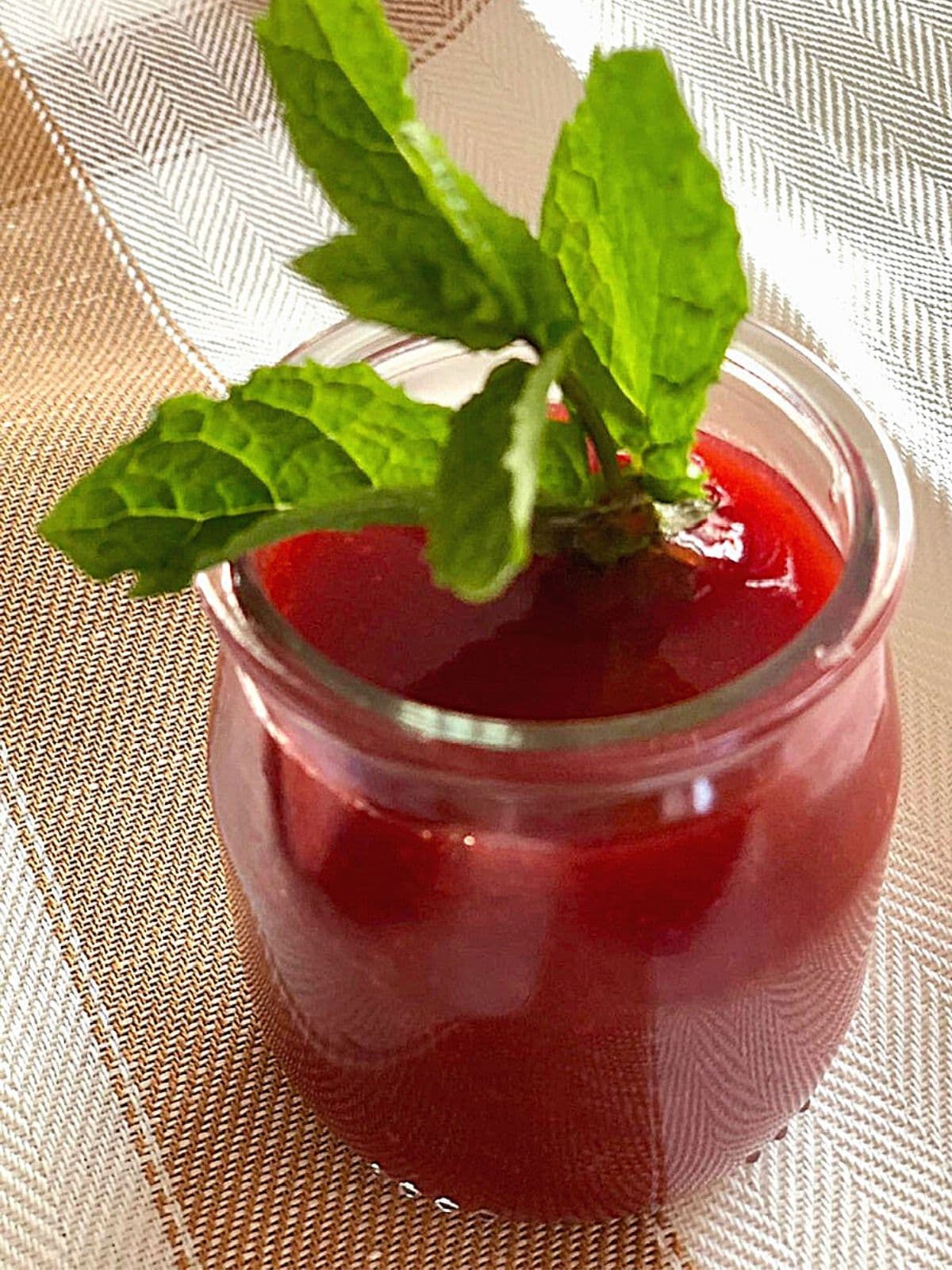Strawberry coulis in a small glass jar with a sprig of mint.