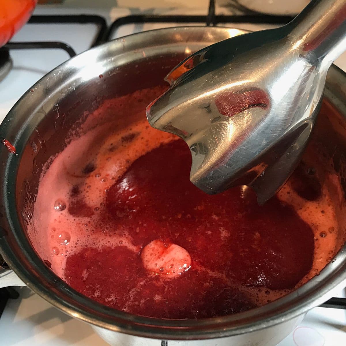 Using hand blender to blend the strawberries in small pan.