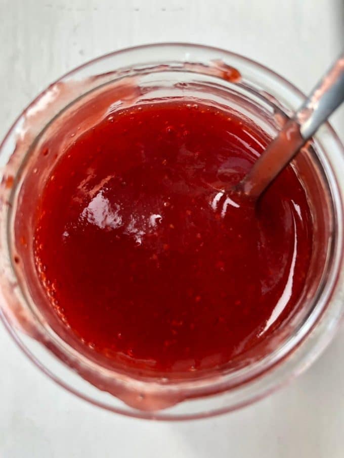 Strawberry coulis in a glass bowl with a metal spoon.