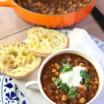 Bowl of soup with sliced bread and large pot of soup