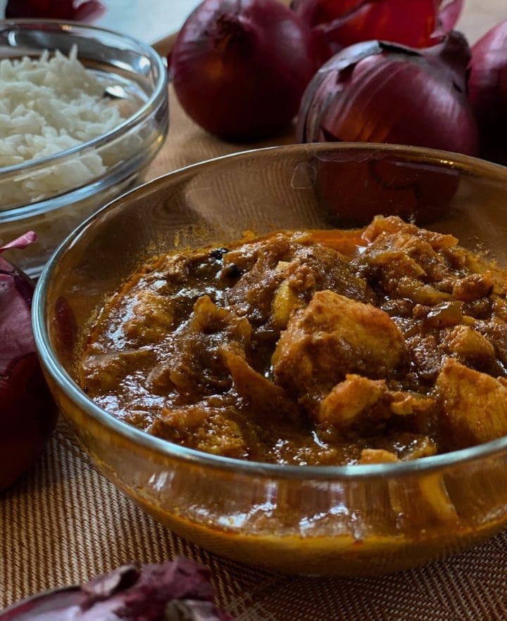 Chicken Do Pyaza in a glass bowl surrounded by ingredients and white rice.