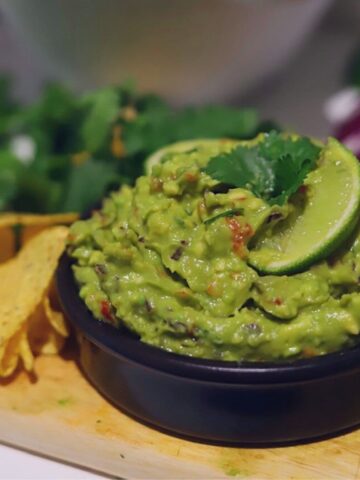 Image of guacamole in small black bowl garnished with cilantro and slice of lime.