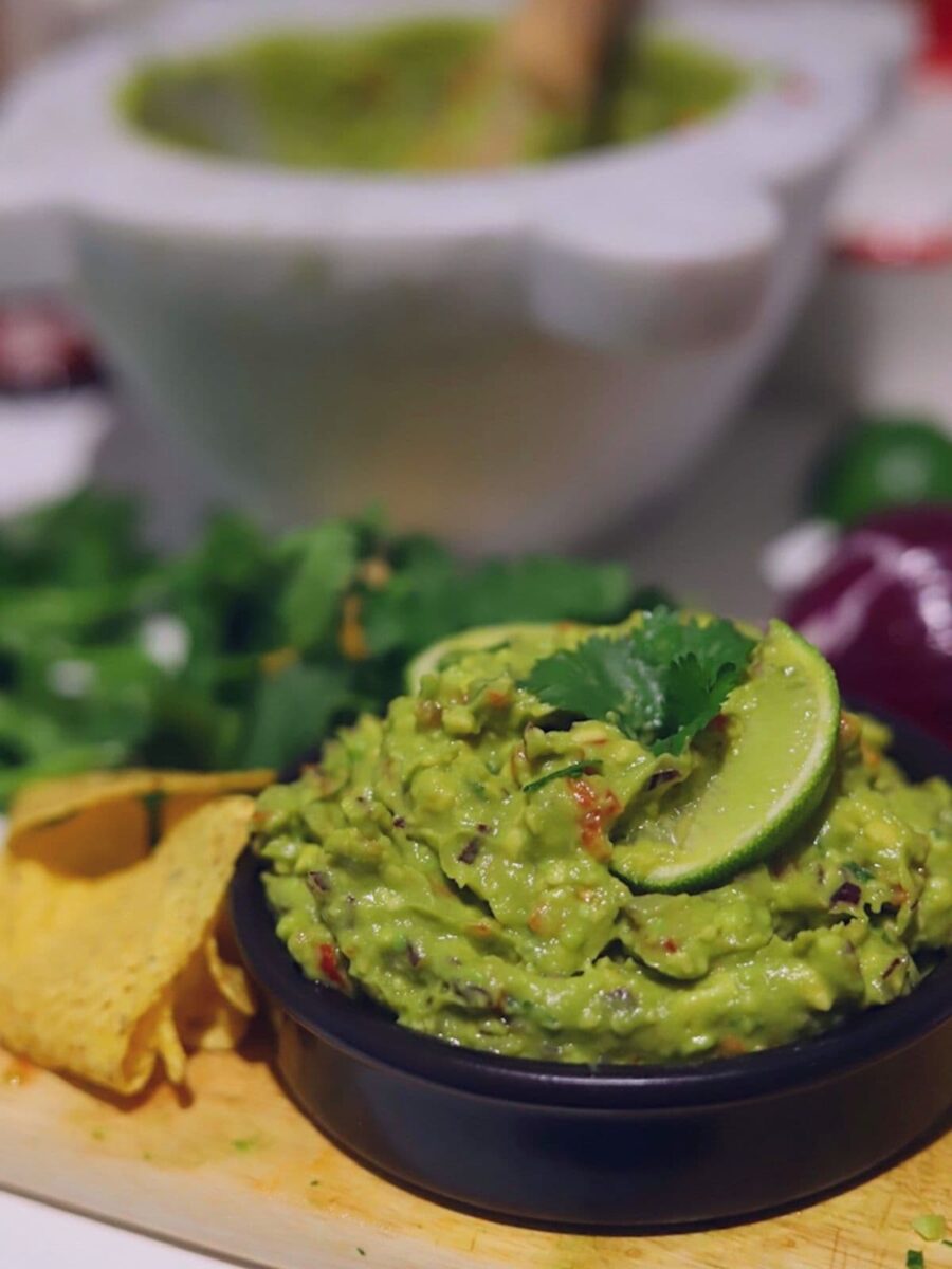 Guacamole in a black bowl surrounded by ingredients