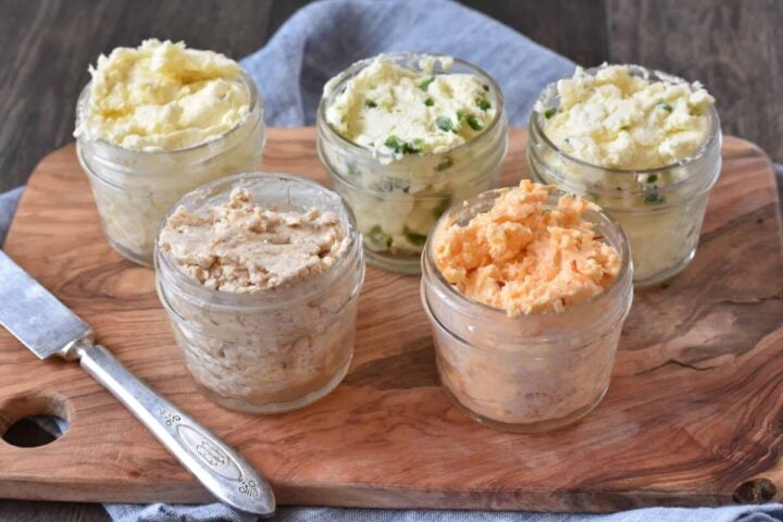 5 butters in small glass jars on wooden board