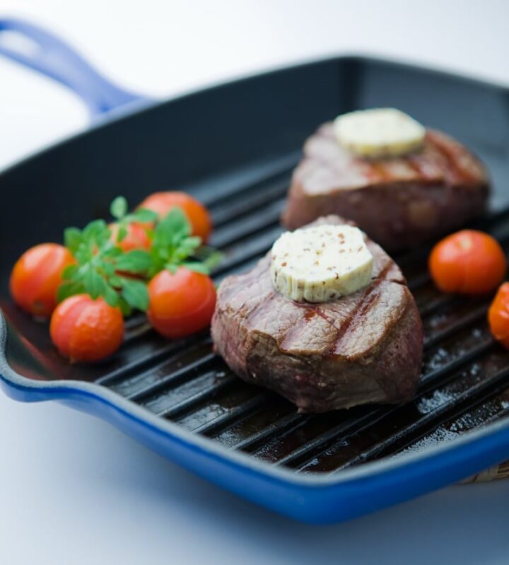 Two steaks in grill pan with rounds of butter on top