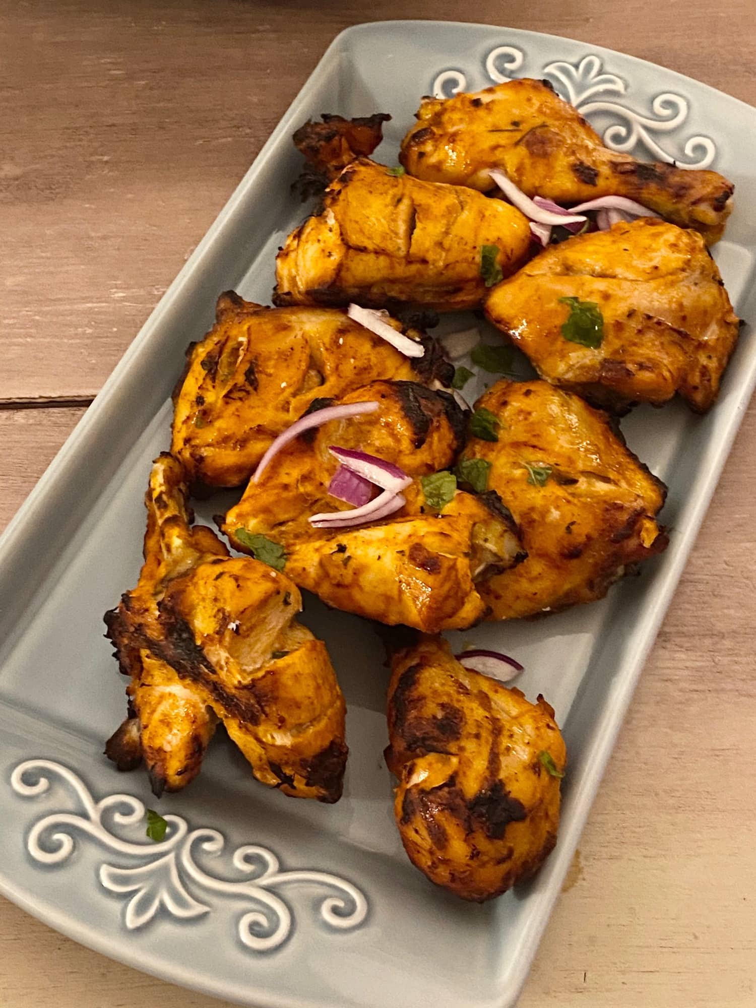 Tandoori chicken garnished with red onions, on a blue platter.