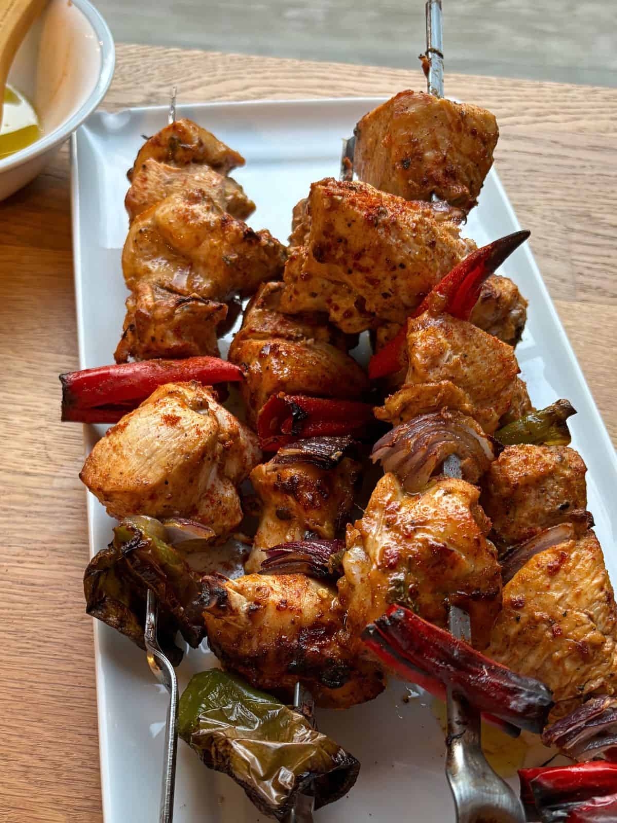 Grilled tandoori chicken,  peppers and onions on a white platter.