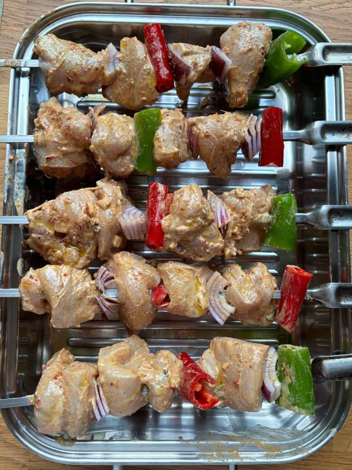 Skewers of marinated chicken with cut peppers and onions on a metal tray ready for grilling.