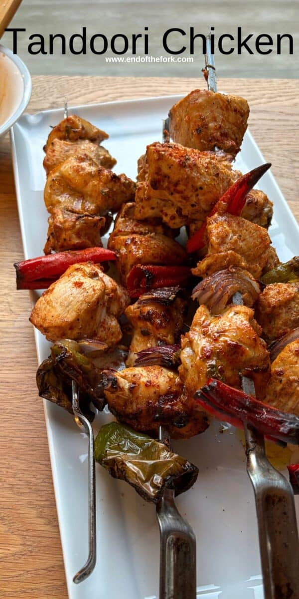 Pin image of tandoori chicken pieces on skewers on white platter.