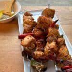 Grilled tandoori chicken, peppers and onions on skewers on a white platter.