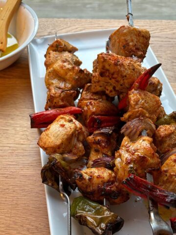 Grilled tandoori chicken, peppers and onions on skewers on a white platter.