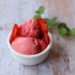 Image of strawberry frozen yogurt with sliced strawberries in white bowl with mint leaves.