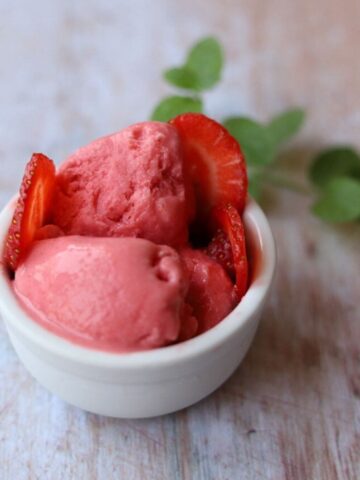 Image of strawberry frozen yogurt with sliced strawberries in white bowl with mint leaves.