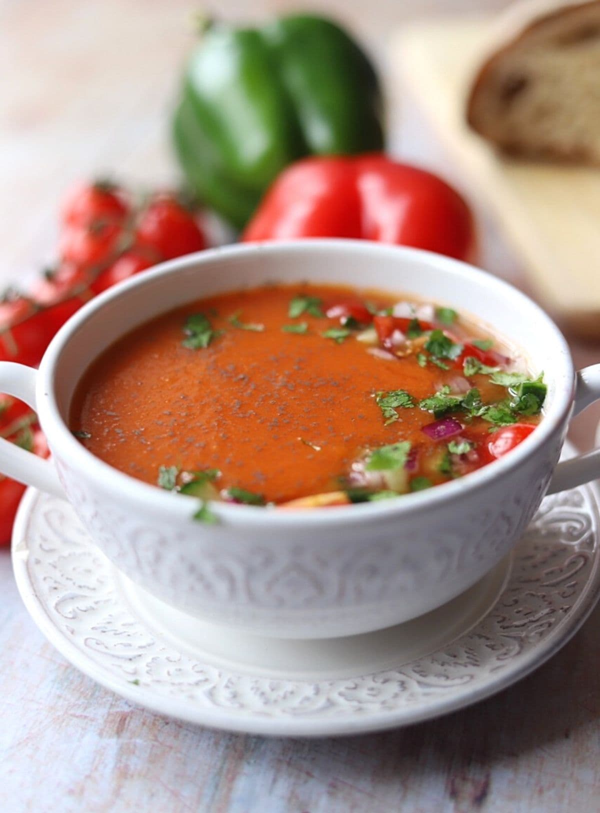 Gazpacho soup in white soup bowl with garnish of parsley and chopped vegetables