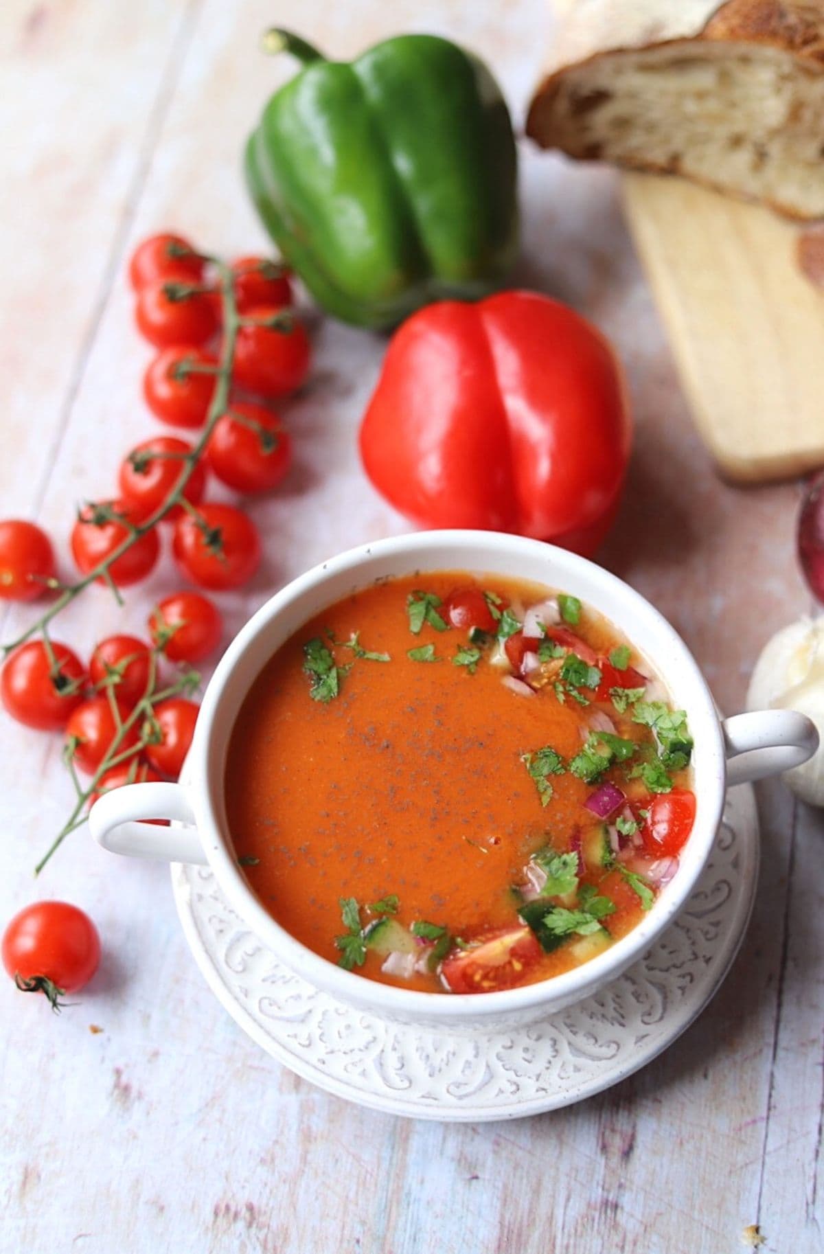 Gazpacho soup surrounded by vegetables on wooden surface