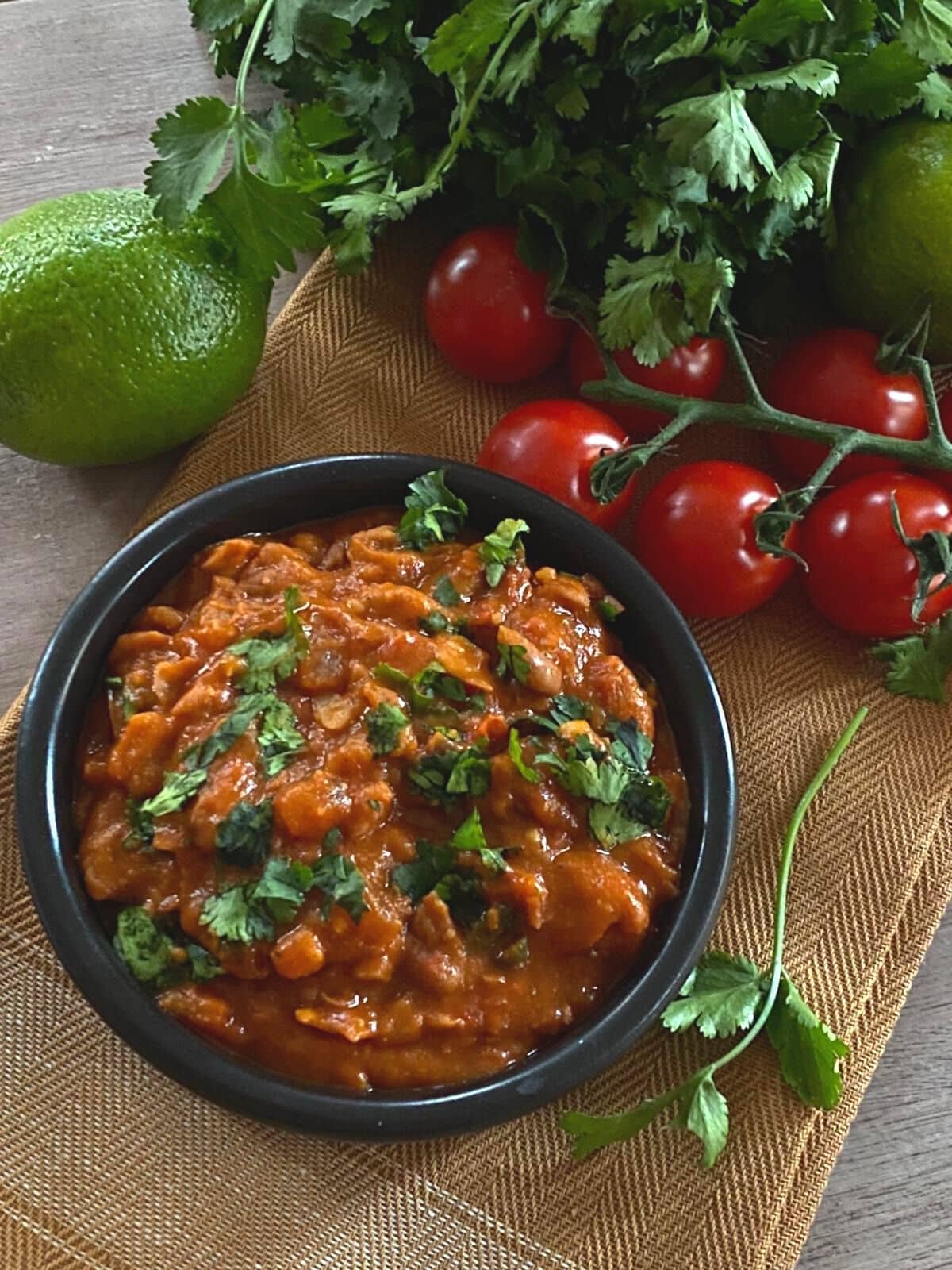 Pinto beans in black bowl flatlay surrounded by limes, herbs tomatoes