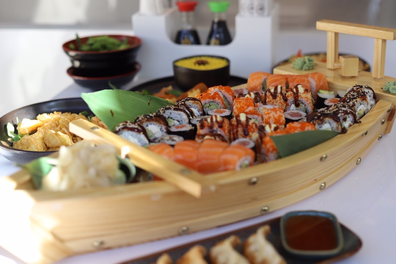 assorted sushi served on small wooden boat on the table