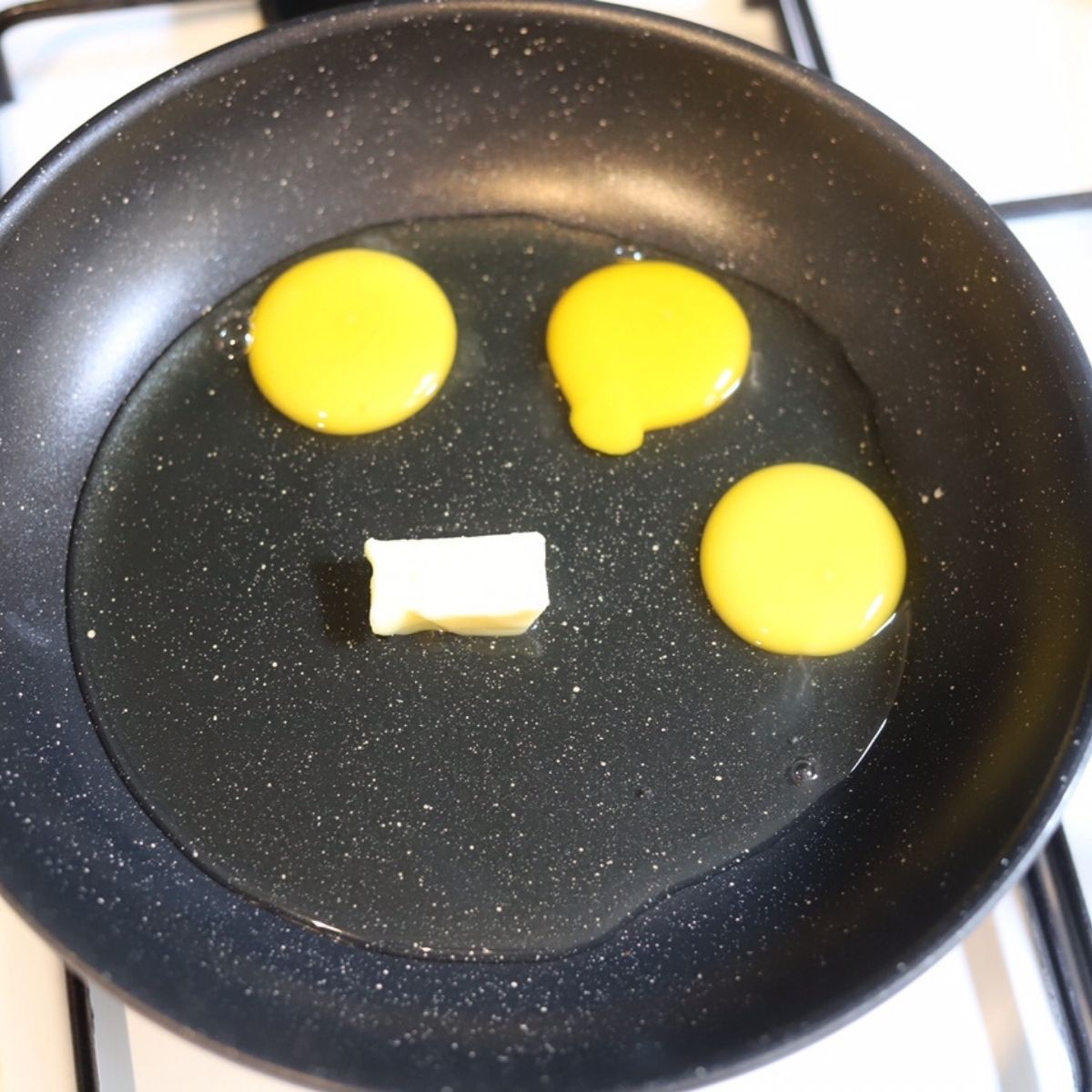 Three raw eggs and butter in a non stick skillet.
