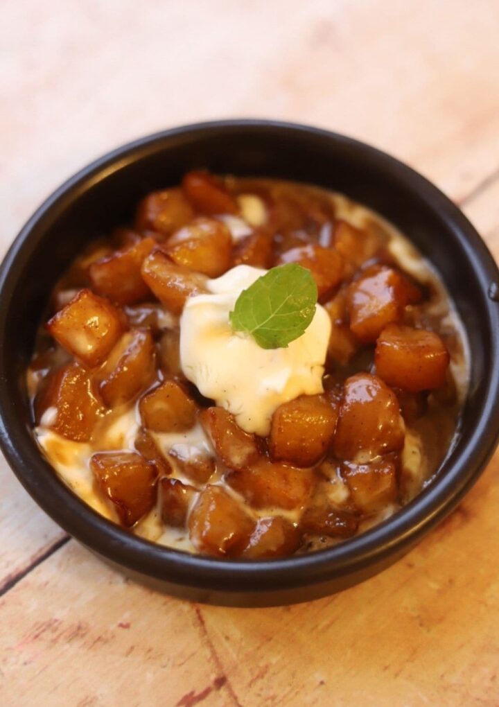 Caramelized apples in black bowl with spoonful of crème fraîche