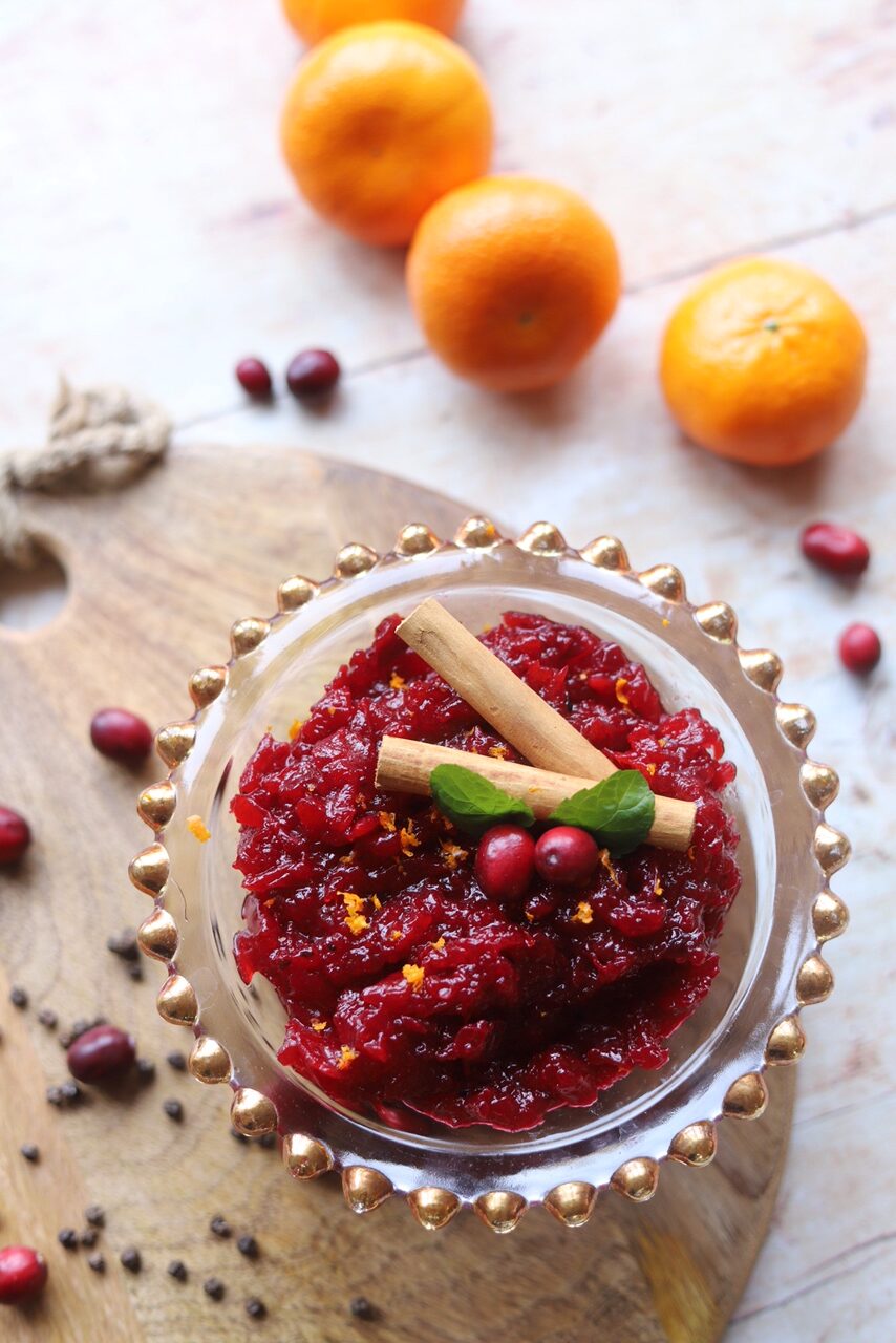 Cranberry sauce in glass bowl alongside oranges and spices