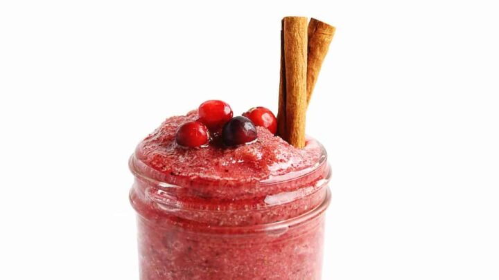 close-up of cranberry smoothie with cranberries on top and two stick cinnamon