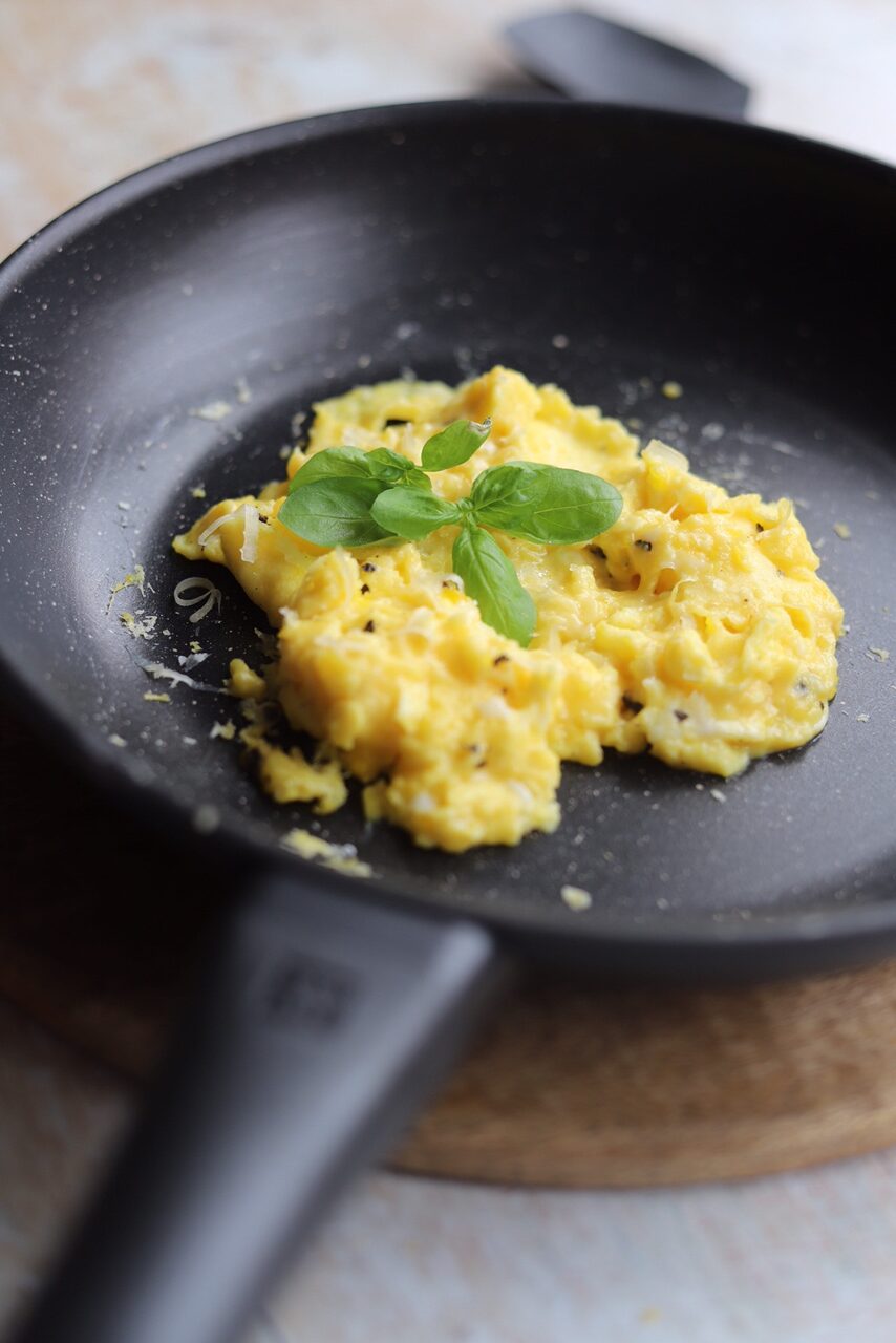 Scrambled eggs in non stick pan with a sprig of basil. 