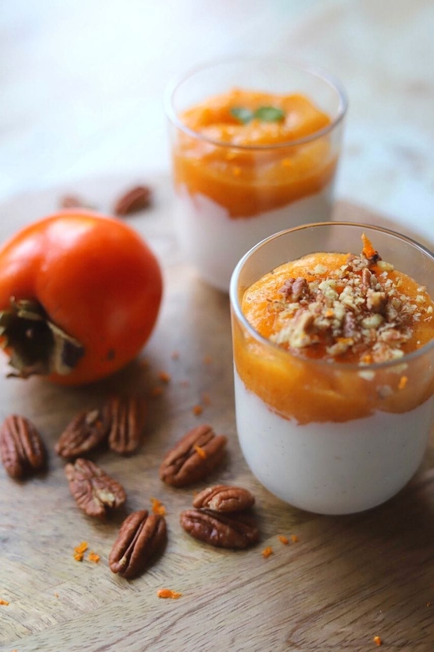 Two glasses of persimmon dessert alongside pecans and a full persimmon.