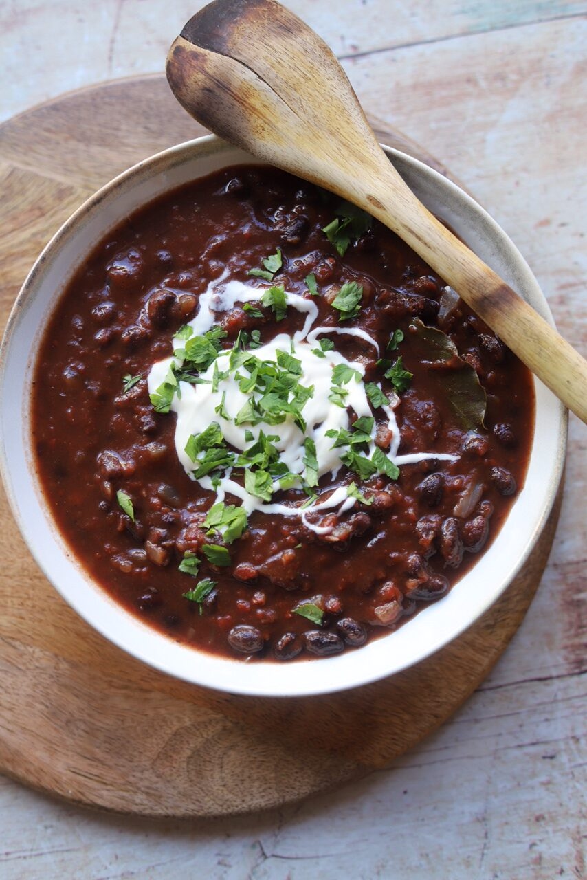 White bowl of black bean stew garnished with sour cream and parsley with wooden spoon.