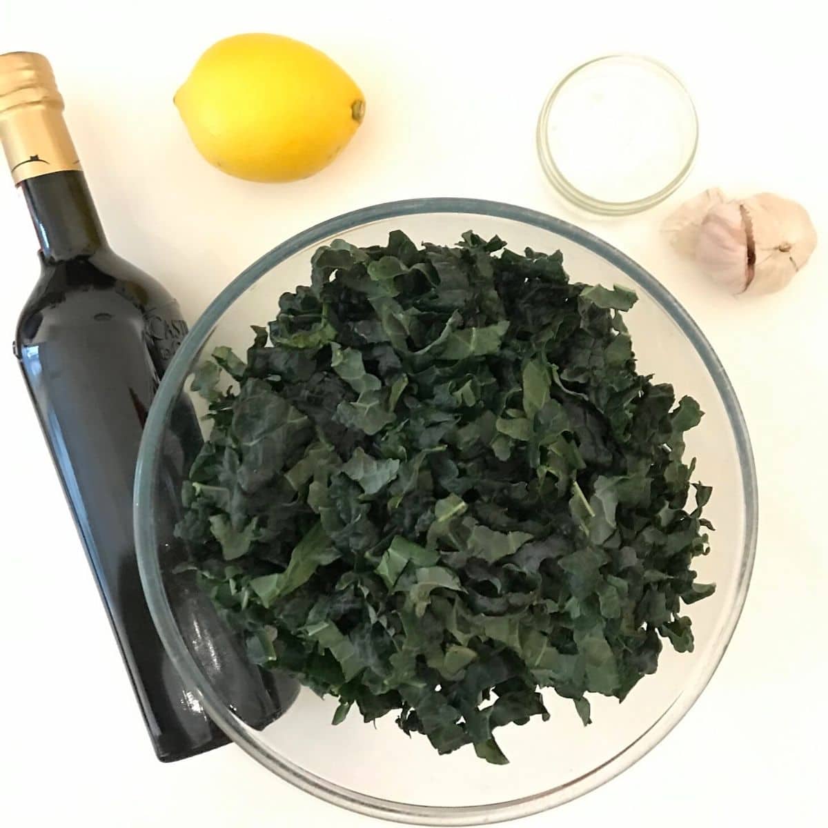 Chopped cavolo nero in glass bowl, bottle of olive oil, a lemon, salt and garlic.