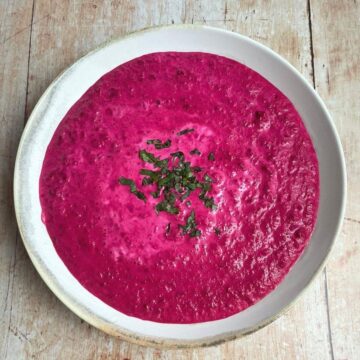 Overhead image of beet soup in white bowl with chopped parsley garnish.