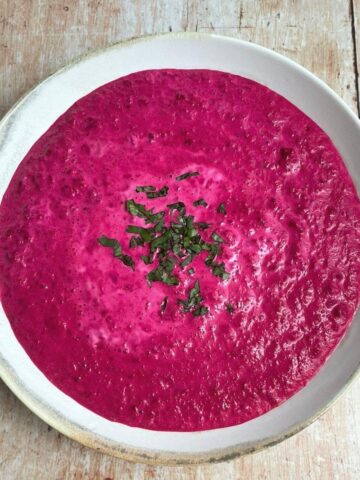 Overhead image of beet soup in white bowl with chopped parsley garnish.