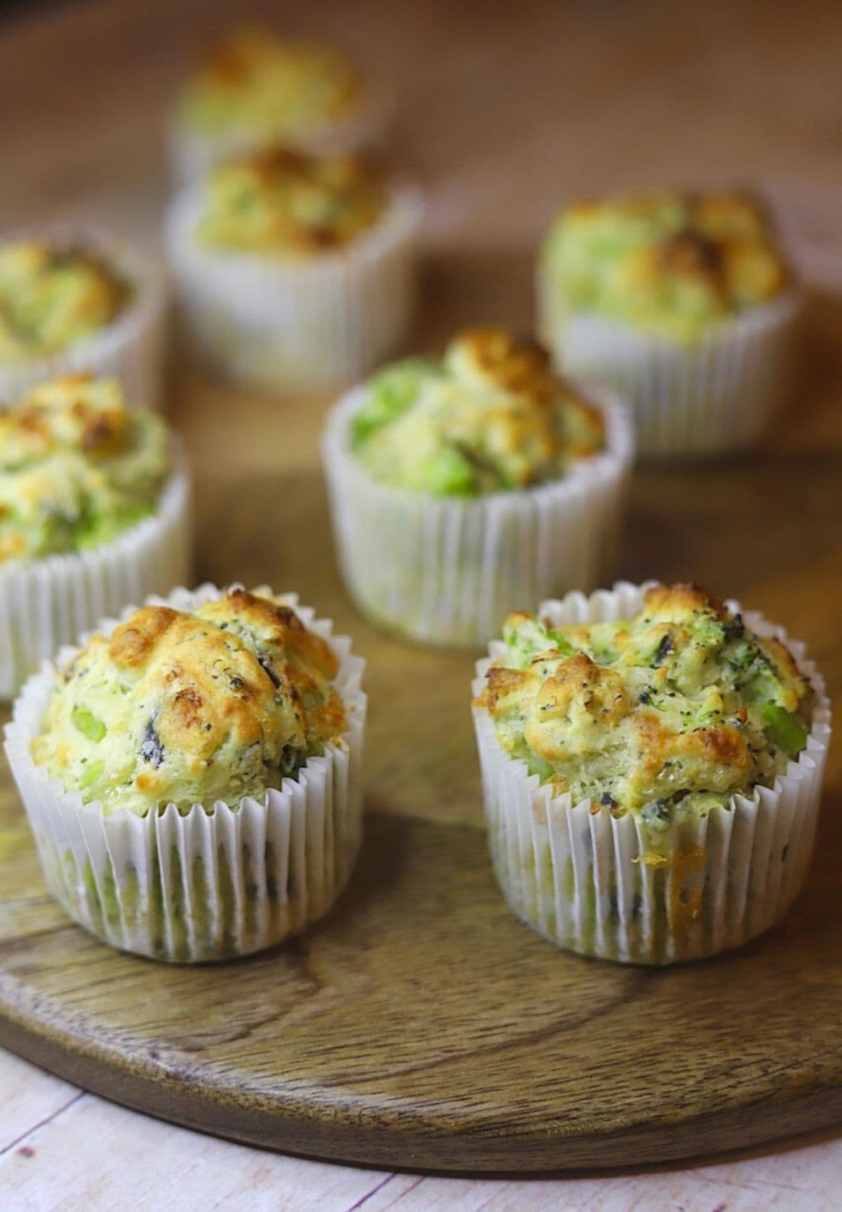 Freshly baked broccoli and cheese muffins in their paper cups on a wooden board.