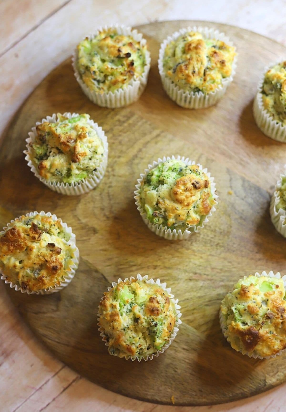 Broccoli and gruyere muffins still in their paper cups on a wooden board.