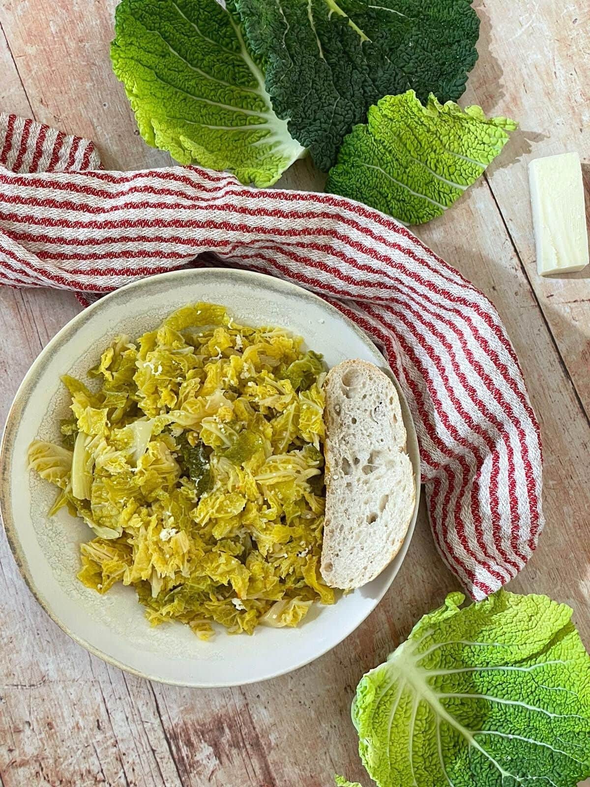 Braised savoy cabbage in a white bowl surrounded by cabbage leaves