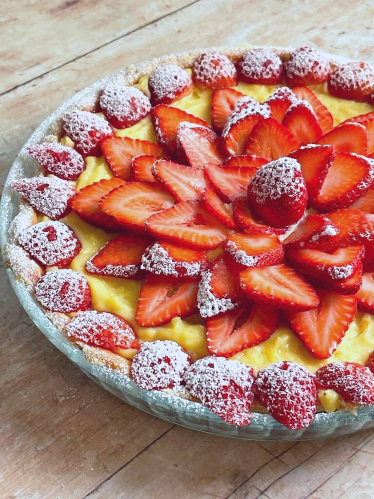 Strawberry tart with custard and a layer of sliced strawberries and powdered sugar.
