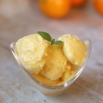 Image of orange frozen yogurt with garnish of basil in a glass bowl.