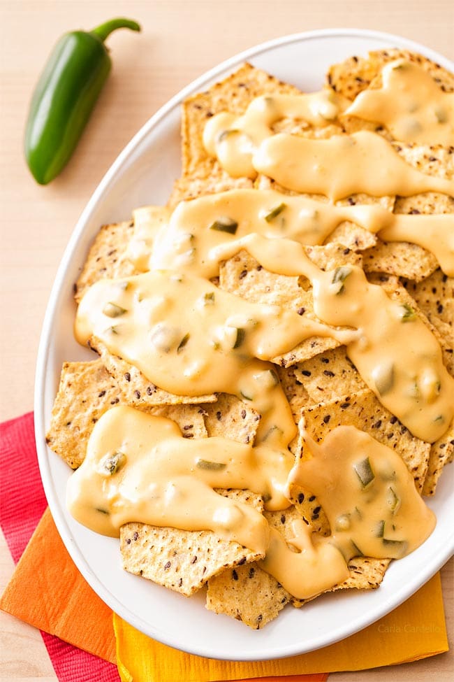 Image of queso sauce over nachos on white platter.