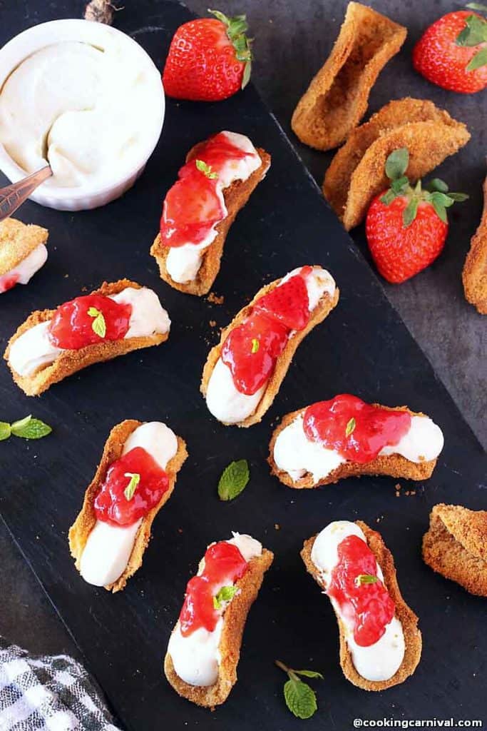 Image of mini strawberry tacos with bowl of cheesecake dip on black platter.