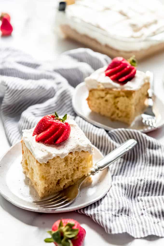 Images of two slices of tres leches cake topped with strawberries on small plates.