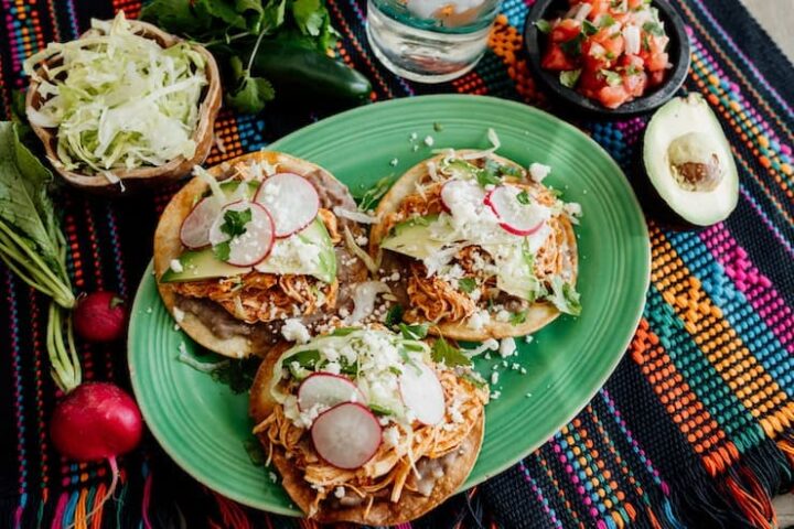 Image of three tortillas with chicken tinga and garnish on a platter.