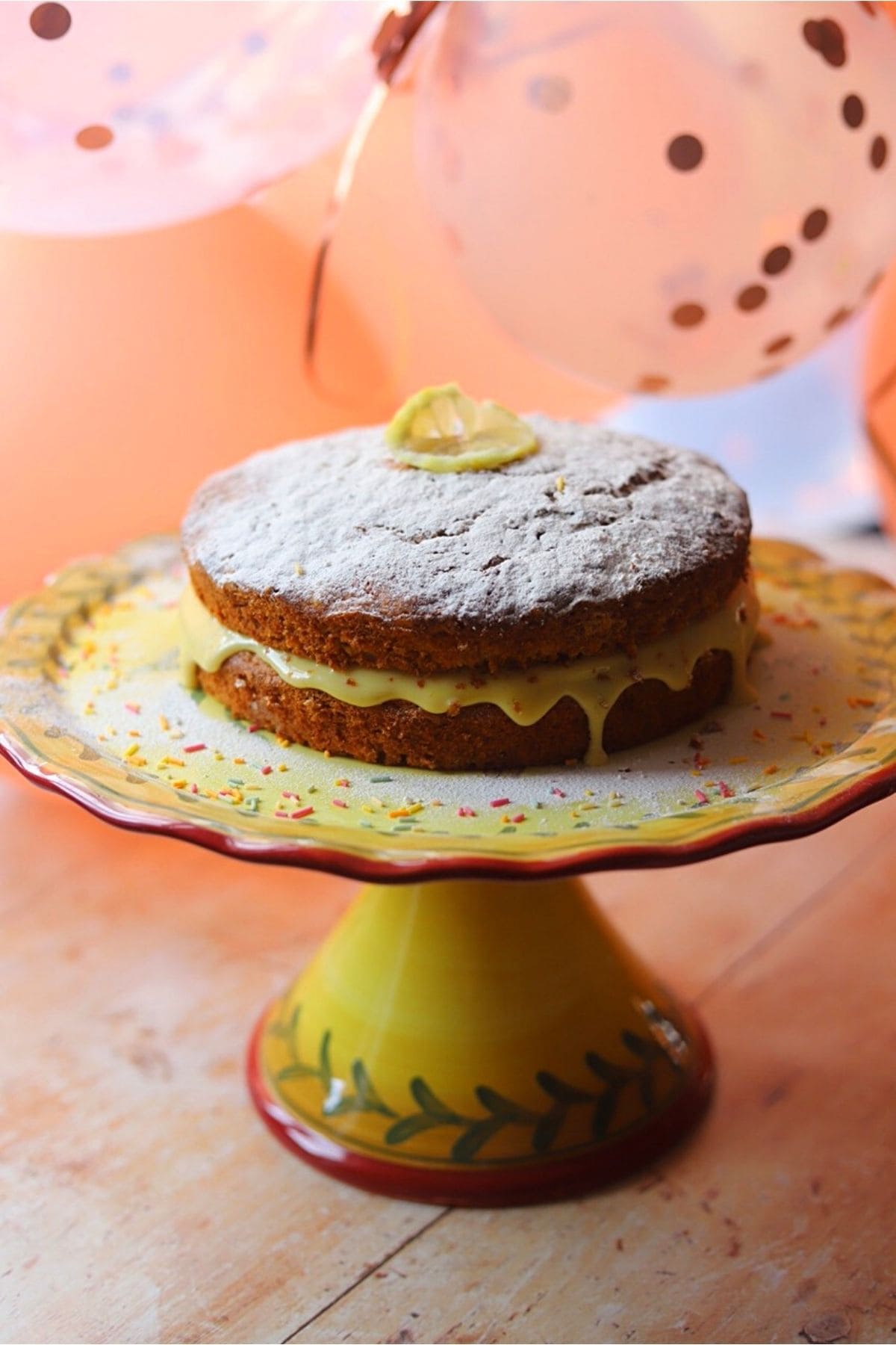 Banana cake on a cake stand, decorated with a slice of lemon and sprinkles.