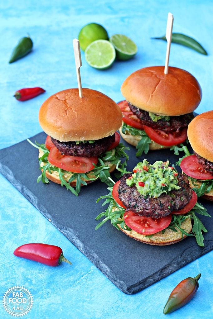 Image of four burgers with guacamole on stone slate.