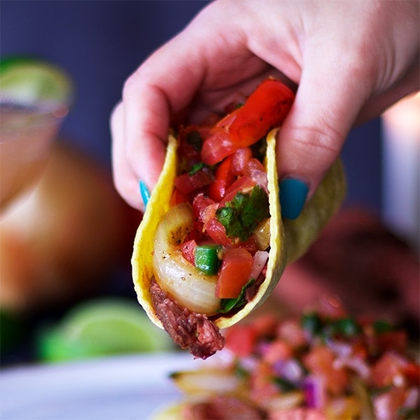 Image of hand lifting a taco filled with steak and pico de gallo.