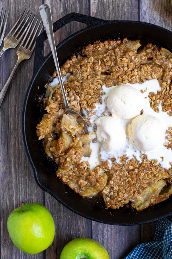 Image of apple crisp topped with three scoops of ice-cream in iron skillet.